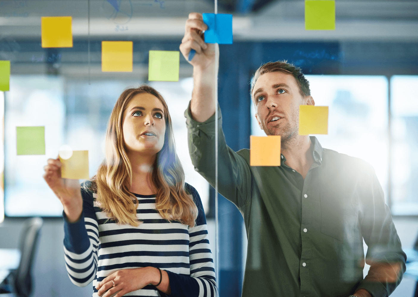 Two people placing sticky notes on a glass board during a brainstorming session