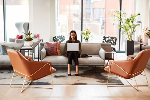 A women sat on a dofa doing work from her laptop