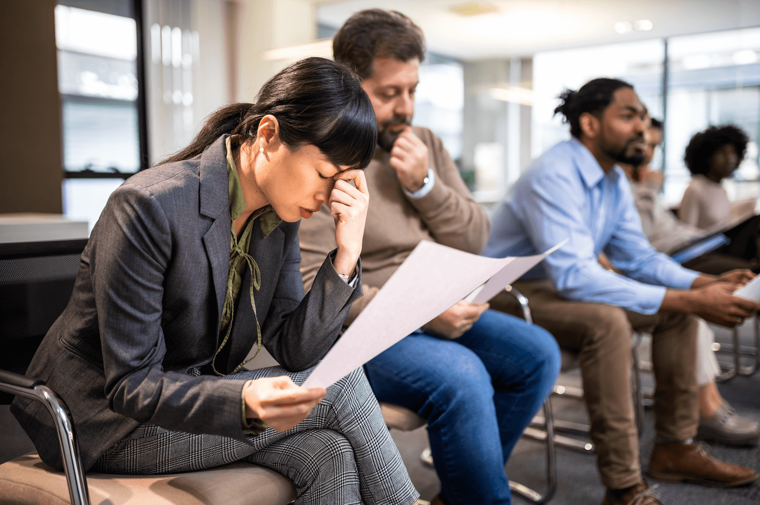 Woman reading a document in a waiting room with other applicants.